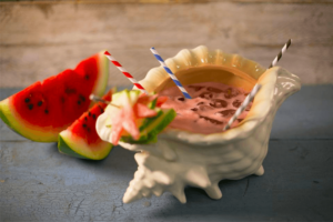 A drink in a conch shell next to a watermelon